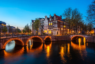 Evening view of a canal with a bridge and illuminated buildings in Amsterdam